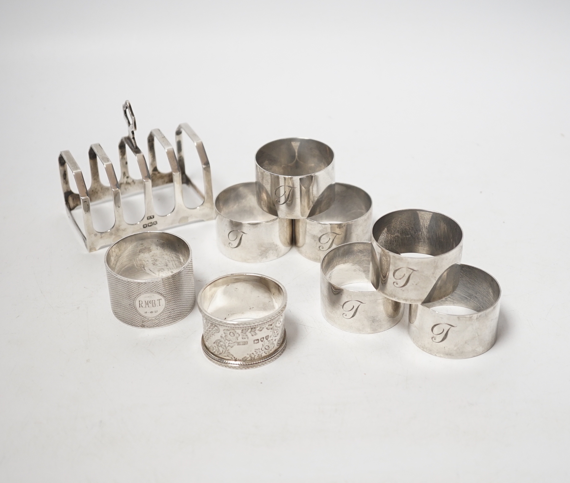 A set of six silver napkin rings, Robert Pringle & Sons, London, 1953, two other silver napkin rings and a silver five bar toast rack, 9.8oz.